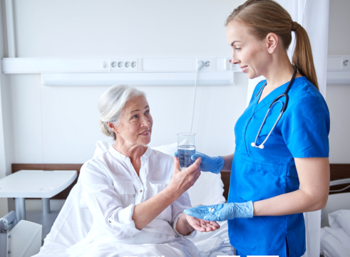nurse assisting old woman in taking medicine
